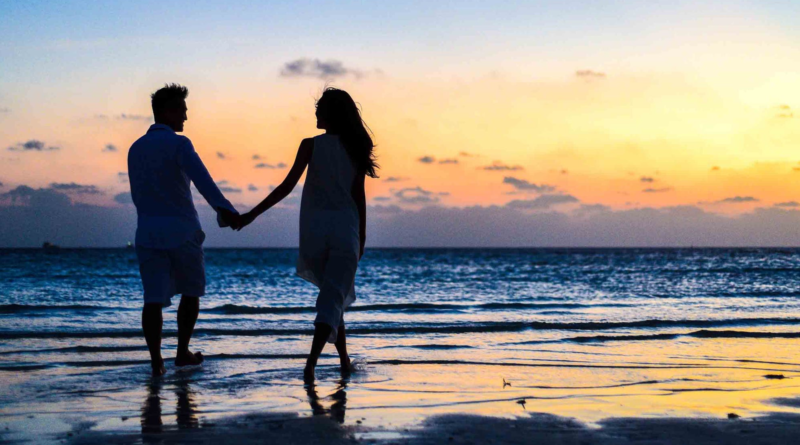 Relacionamentos pelo ponto de vista de Ifa. Casal anda de mãos dadas na praia no pôr do sol.